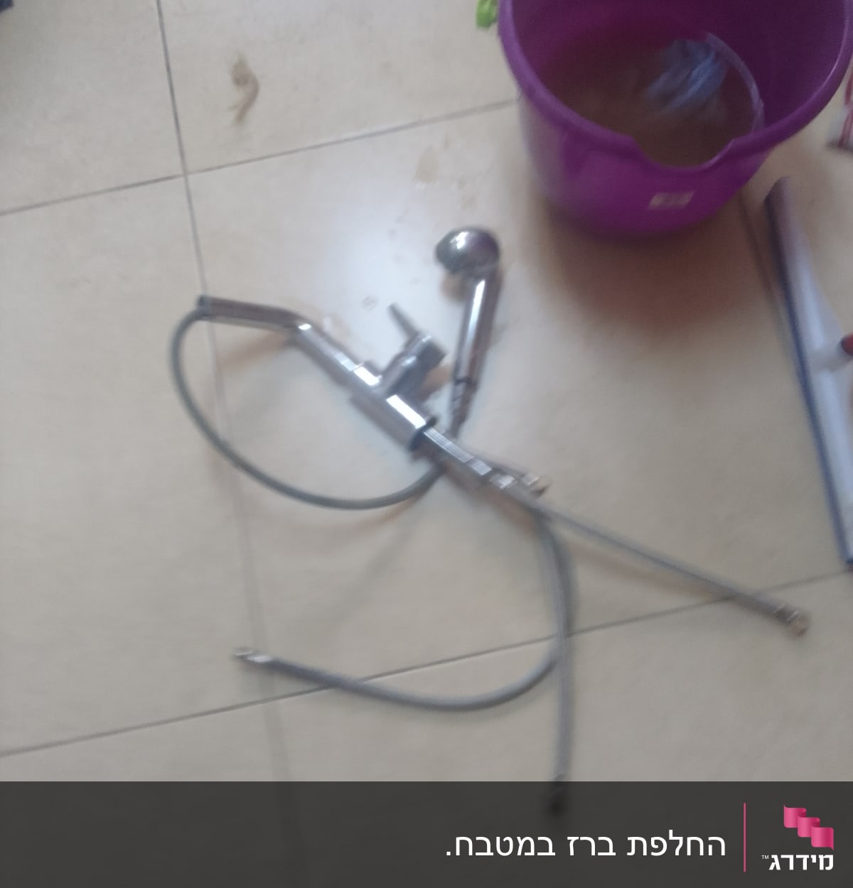 ברז וכבל מים על רצפה ליד דלי סגול